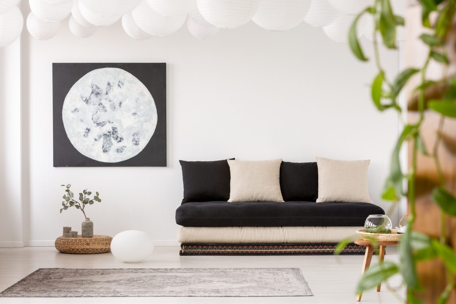 Pillows on black sofa in white living room interior with moon poster and grey carpet